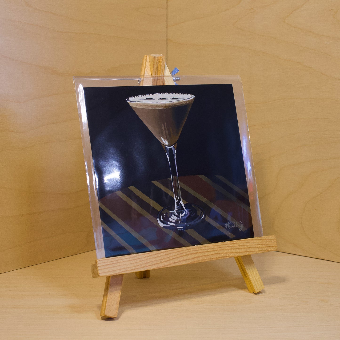 A 6x6" fine art print of the original acrylic painting "Espresso Martini" by Hannah Kilby from Hannah Michelle Studios. Displayed in a protective plastic sleeve on a small, wooden easel.