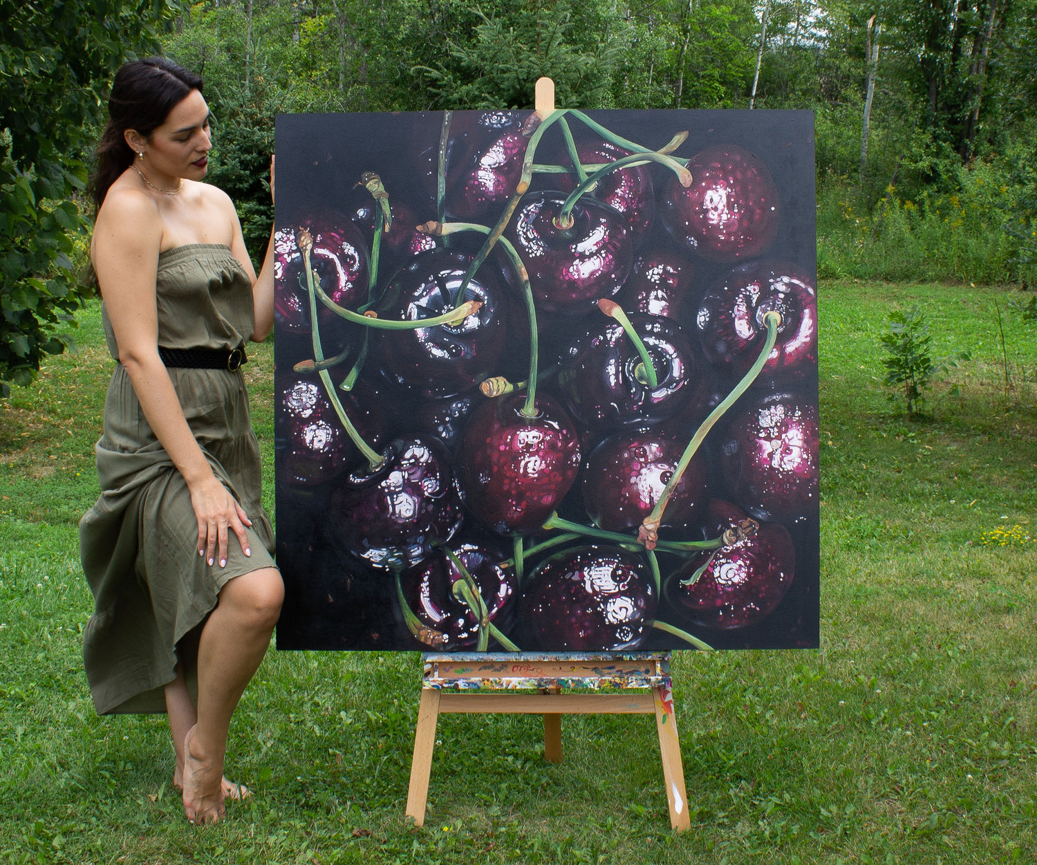Artist, Hannah Kilby, stands next to her original painting "Cherries".
