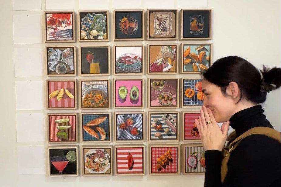 Person standing in a room with a wall displaying a grid of small framed pictures.