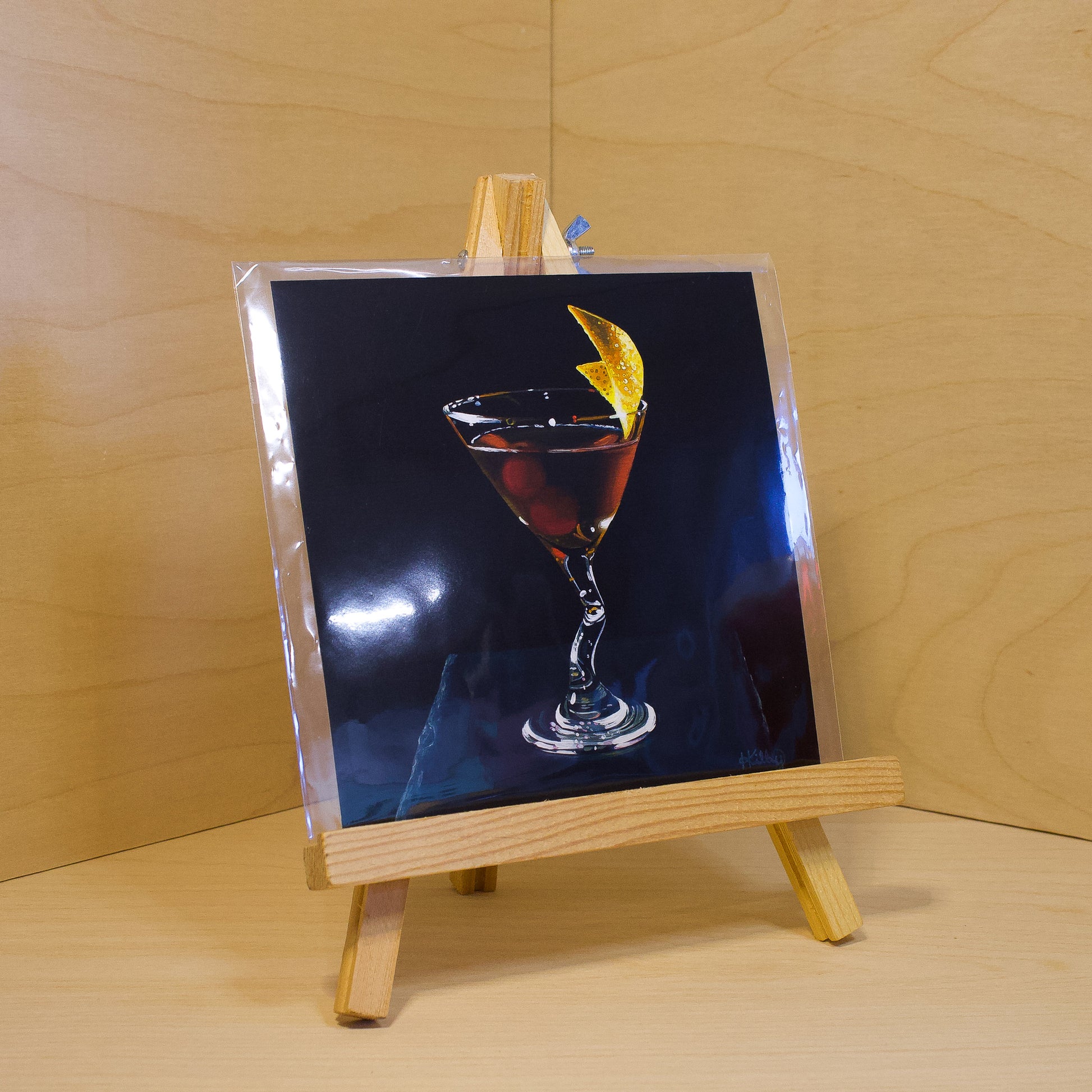 A 6x6" fine art print of the original acrylic painting "Manhattan" by Hannah Kilby from Hannah Michelle Studios. Displayed in a protective plastic sleeve on a small, wooden easel.