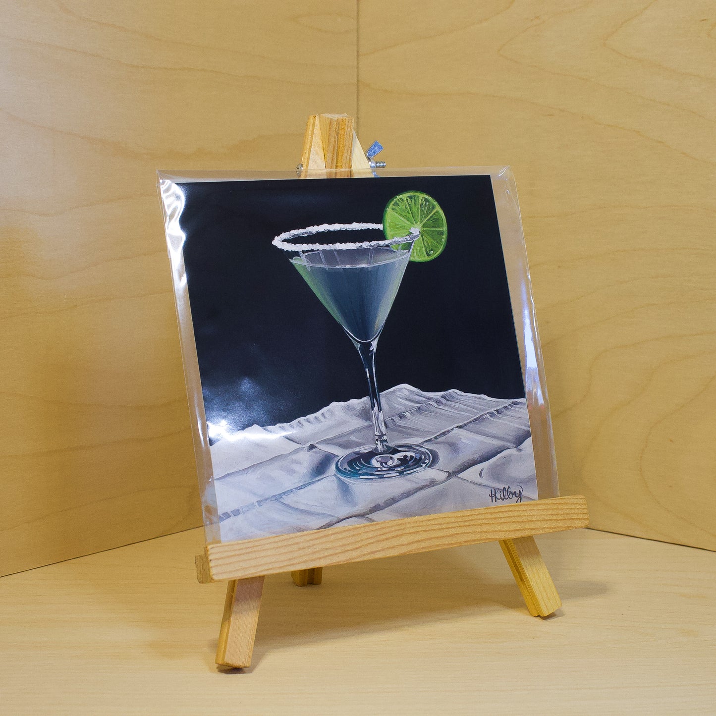 A 6x6" fine art print of the original acrylic painting "Margarita" by Hannah Kilby from Hannah Michelle Studios. Displayed in a protective plastic sleeve on a small, wooden easel.